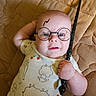 baby, child, costume, cute, expression, face, glasses, hand, indoor, infant, lightning_bolt, lying_down, magic, onesie, playful, portrait, quilted_blanket, sheep_pattern, wand, young