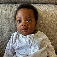 Liam is registered to the contest to win money with this photo: baby, child, infant, onesie, clothing, face, expression, couch, fabric, pattern, herringbone, texture, curious, portrait, indoor, seated, young, cute, person, cozy