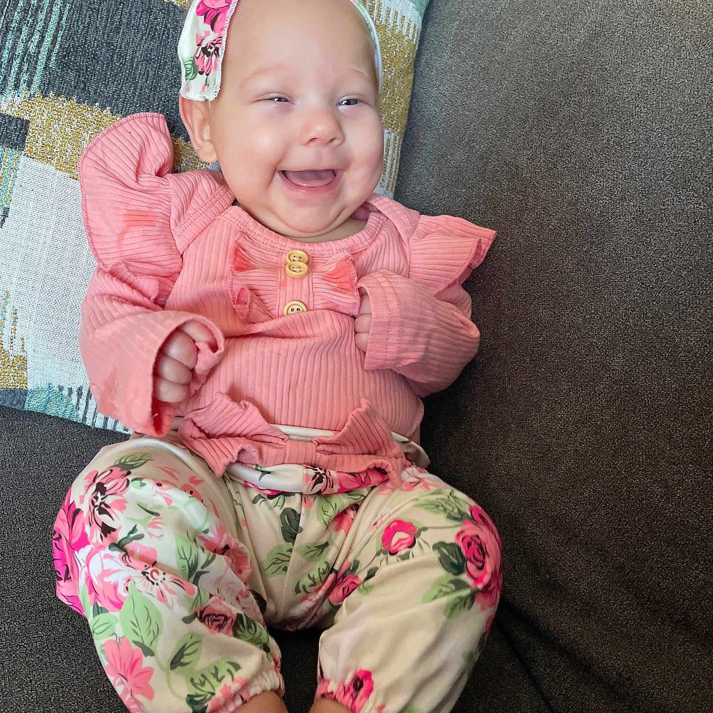 Hazel is registered to the contest to win money with this photo: baby, child, comfortable, couch, cute, feet, floral_pants, happy, headband, home, indoors, infant, patterned_clothing, pillow, pink_clothing, portrait, ribbons, sitting, smiling, young_child