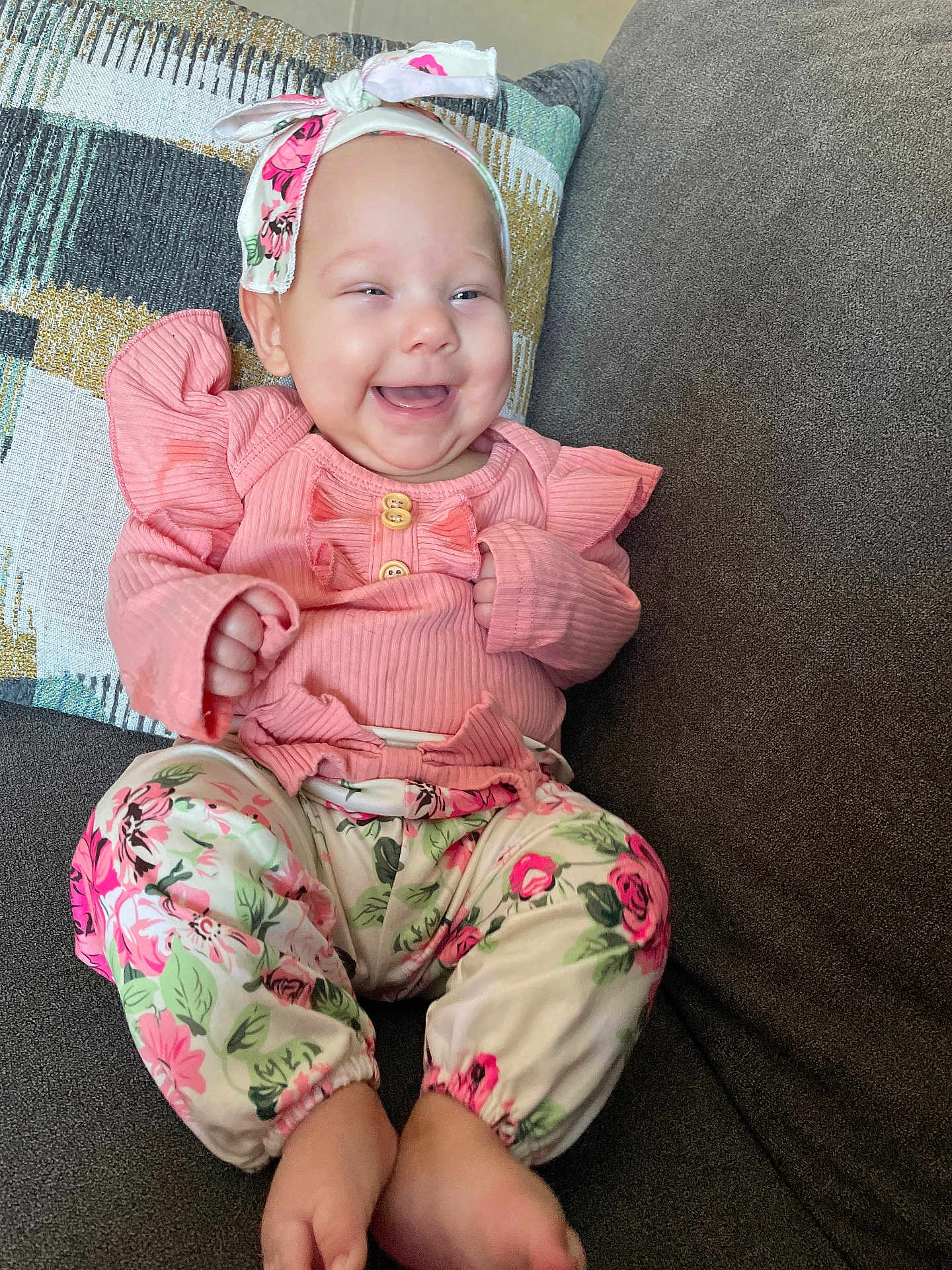 Hazel is registered to the contest to win money with this photo: baby, child, comfortable, couch, cute, feet, floral_pants, happy, headband, home, indoors, infant, patterned_clothing, pillow, pink_clothing, portrait, ribbons, sitting, smiling, young_child