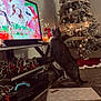 Norman joined the competition — help win amazing prizes! candle, carpet, cat, christmas_tree, festive_decor, game_controller, holiday_music, holly, living_room, ornaments, people_on_screen, pet, presents, ribbon, shelf, standing_cat, string_lights, television, tv_screen, wrapped_gifts