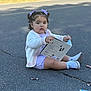 toddler, child, book, road, asphalt, candy, wrapper, shoes, sneakers, clothing, hair_bows, outdoor, sitting, curly_hair, white_cardigan, purple_outfit, person, daylight, cute, playful