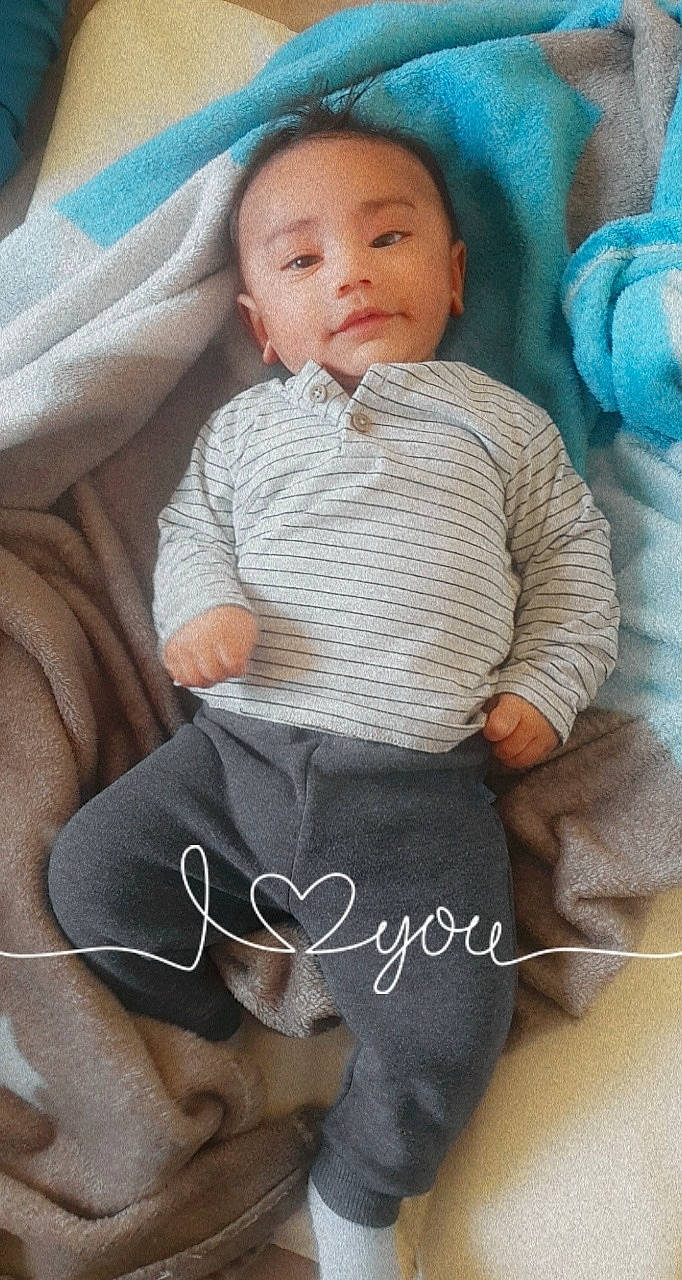 Ryan participe au concours pour gagner de l'argent avec cette photo : arm, baby, baby_toddler_clothing, blue, cheek, comfort, eye, hand, headgear, human_body, knee, leg, linens, neck, person, skin, sleeve, textile, thigh, toddler