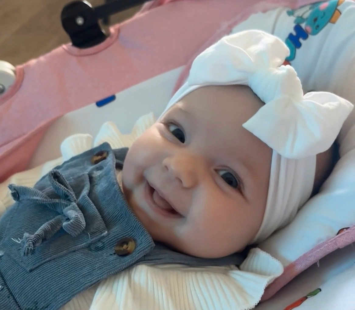 Ambre a rejoint le concours — aidez-le/la à gagner de superbes lots ! baby, infant, smiling, headband, bow, cheeks, eyes, closeup, portrait, denim, overalls, buttons, baby_seat, blanket, pink, clothing, adorable, indoor, soft_lighting, happy