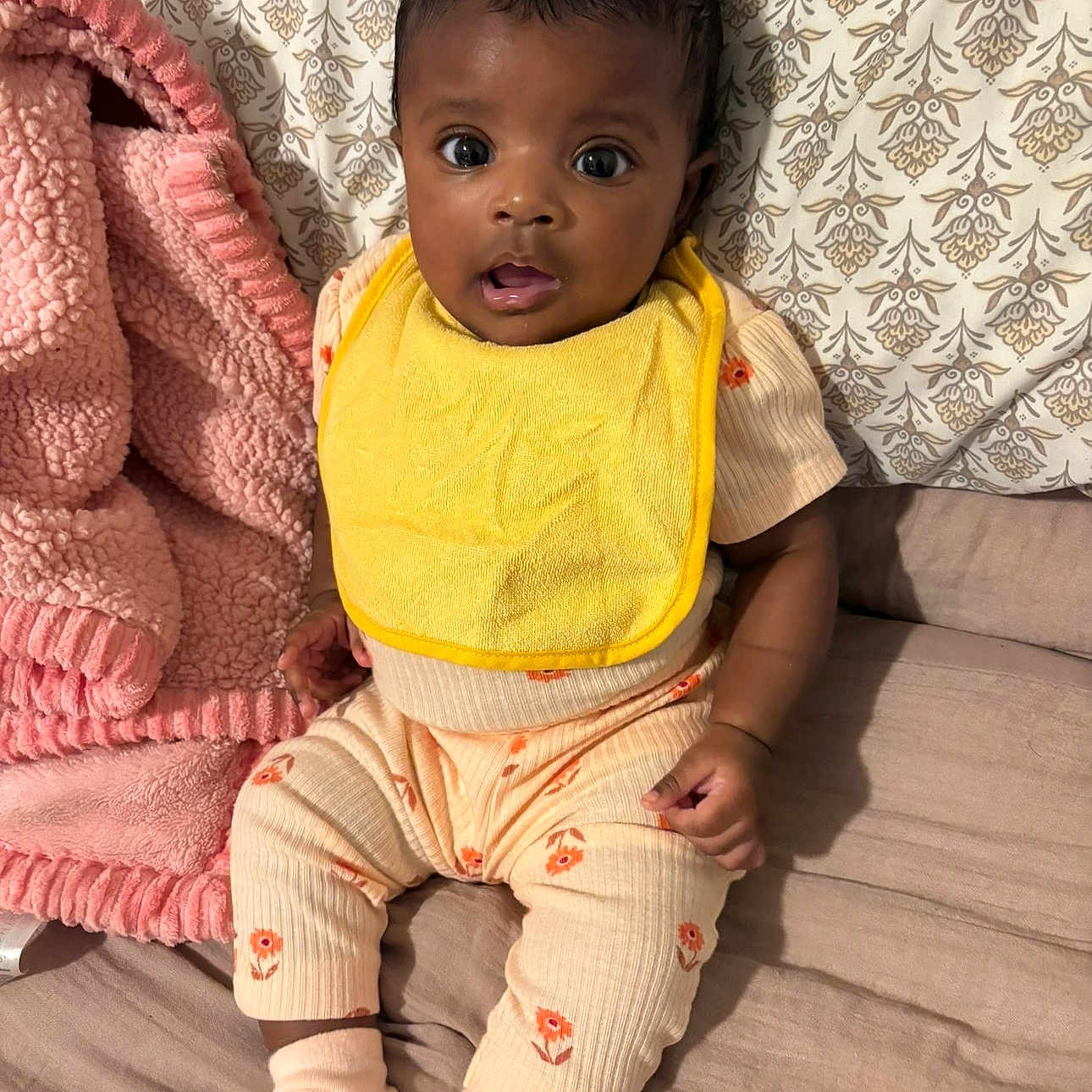 Yaelanni is registered to the contest to win money with this photo: baby, child, yellow_bib, pink_blanket, patterned_pillow, bed, sitting, curious_eyes, cozy, indoors, clothing, sock, infant, cute, portrait, small_hands, looking_up, soft_texture, fabric, resting