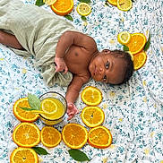 Zayden is registered to the contest to win money with this photo: baby, infant, orange_slices, lemon_slices, citrus, juice, glass, leaf, blanket, floral_pattern, wrapped, lying_down, curious, looking_at_camera, fresh, summer, fruit, drink, child, indoors