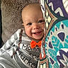 Ean is registered to the contest to win money with this photo: baby, child, infant, smiling, happy, portrait, close_up, indoors, blanket, fabric, bow_tie, gray_clothing, patterned_blanket, brown_eyes, face, head, sitting, cozy, home, photography