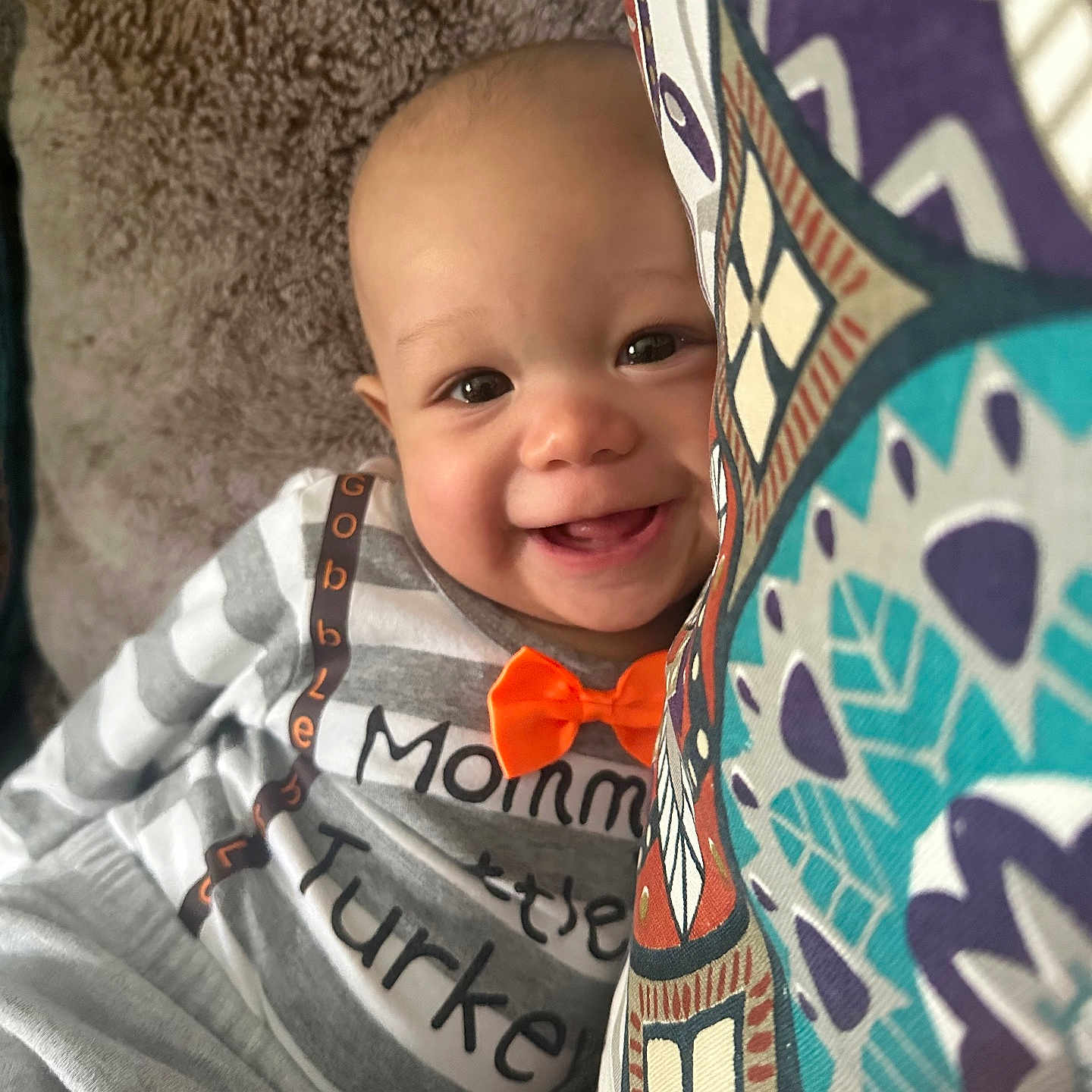 Ean is registered to the contest to win money with this photo: baby, child, infant, smiling, happy, portrait, close_up, indoors, blanket, fabric, bow_tie, gray_clothing, patterned_blanket, brown_eyes, face, head, sitting, cozy, home, photography
