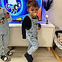 Aly participe au concours pour gagner de l'argent avec cette photo : child, toddler, denim_overalls, mickey_mouse, pacifier, black_shoes, living_room, tv_screen, flooring, modern_furniture, baby_rocker, playful_pose, indoor, person, clothing, toy, decor, plant, sneakers, casual_wear