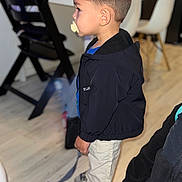 Aly participe au concours pour gagner de l'argent avec cette photo : toddler, child, pacifier, jacket, pants, indoor, floor, chair, table, footwear, side_view, short_hair, modern_interior, wood_floor, blurry_background, standing, person, young_child, looking_sideways, casual_clothing