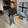 child, boy, indoor, floor, jeans, sweatshirt, toy, wooden_toy, activity_cube, play_tent, stroller, socks, casual_clothing, young_child, playing, light_wood_floor, curious, seated, home, portrait