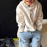 Djibryl a rejoint le concours — aidez-le/la à gagner de superbes lots ! child, boy, smiling, standing, indoor, shirt, striped_shirt, jeans, baggy_jeans, black_shoes, casual_clothing, happy, hands_in_pockets, floor, television, blurred_background, home_interior, furniture, light_wood_floor, portrait