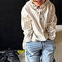 child, boy, smiling, standing, indoor, shirt, striped_shirt, jeans, baggy_jeans, black_shoes, casual_clothing, happy, hands_in_pockets, floor, television, blurred_background, home_interior, furniture, light_wood_floor, portrait