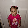 child, girl, smiling, pink_clothing, braided_hair, pigtails, indoor, door, carpet, standing, cute, portrait, young_child, casual_wear, happy, fashion, person, hair_accessory, graphic_tshirt, toddler