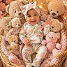 baby, teddy_bear, basket, plush_toy, headband, pajamas, smiling, child, soft_lighting, indoors, cozy, pink, warm_colors, flower_background, cute, happy, portrait, sitting, blanket, decor
