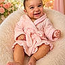 baby, child, smiling, pink_robe, furry_chair, soft_lighting, fairy_lights, flowers, happy, cute, portrait, indoors, cozy, warm_colors, infant, sitting, skin, head, hands, feet