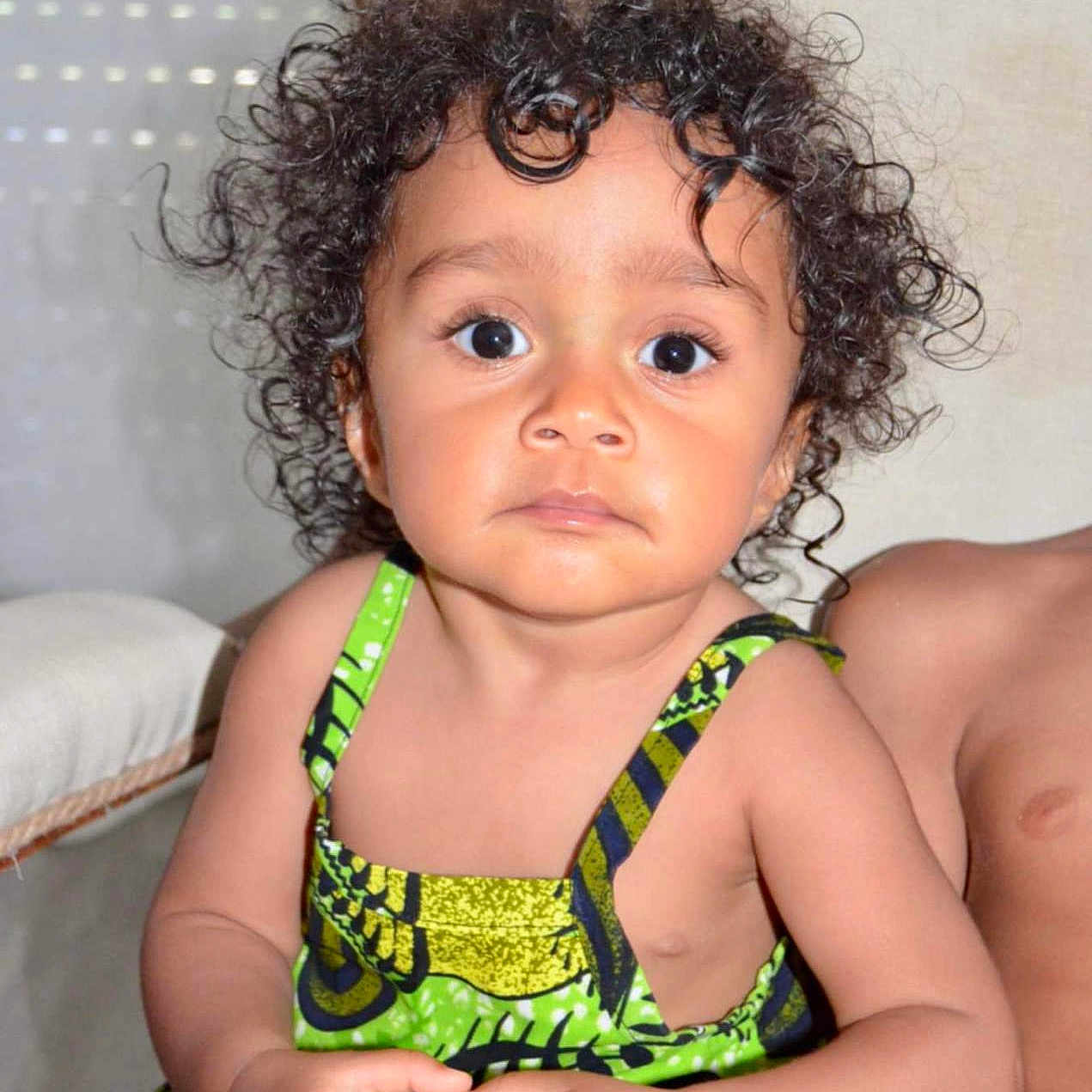 Mia a rejoint le concours — aidez-le/la à gagner de superbes lots ! background, casual, child, clothing, curly_hair, cute, expression, eyes, face, green_dress, hands, indoor, natural_light, person, portrait, seat, sitting, skin, toddler, young_child