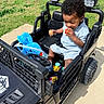 Willie joined the competition — help win amazing prizes! toddler, child, toy_car, outdoor, grass, concrete, sunlight, plastic_eggs, stuffed_animal, candy, black_toy_car, seatbelt, shorts, shirt, curly_hair, playtime, sidewalk, daytime, vehicle, young_child