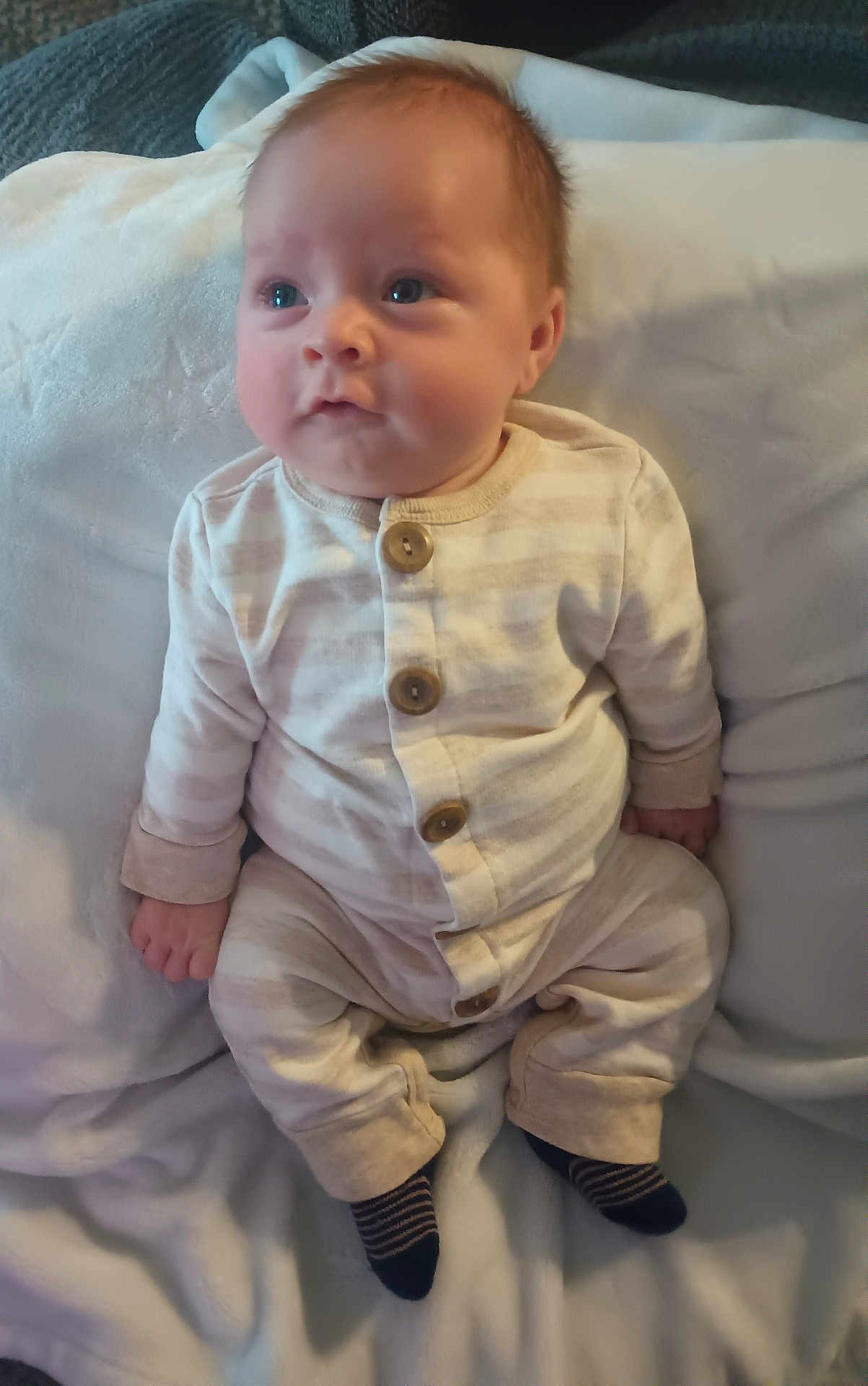 Levi is registered to the contest to win money with this photo: baby, infant, pajamas, striped_clothing, blanket, soft_fabric, cute, sitting, indoors, child, person, young, cozy, portrait, small_hands, face, head, feet, socks, sleepwear