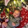 Ronan is registered to the contest to win money with this photo: baby, christmas_tree, holiday_decorations, teddy_bear, snowflake_pattern, tree_skirt, smiling, infant, festive, toy, indoor, holiday, christmas, green_clothing, decor, seasonal, face, person, cute, playful