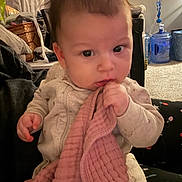 Caruso joined the competition — help win amazing prizes! baby, blanket, indoor, child, person, face, clothing, hand, carpet, water_bottle, basket, chair, couch, soft_toy, curious, young_child, seated, expression, home, cozy