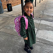 Demi is registered to the contest to win money with this photo: child, girl, backpack, green_dress, braids, bow, sidewalk, concrete, outdoor, smiling, black_boots, pink, happy, school, person, urban, daylight, brick_wall, casual, portrait