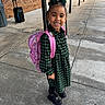 child, girl, backpack, green_dress, braids, bow, sidewalk, concrete, outdoor, smiling, black_boots, pink, happy, school, person, urban, daylight, brick_wall, casual, portrait