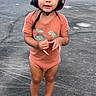 barefoot, casual_clothing, child, curious, cute, daylight, dinosaur, expression, headgear, helmet, onesie, outdoor, pavement, person, playful, small_person, smile, standing, toddler, young_child