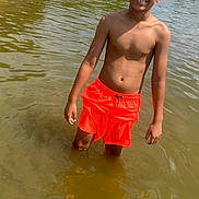 Kaide is registered to the contest to win money with this photo: barefoot, boy, casual, child, daytime, greenery, lake, nature, outdoor, pond, sandy_bank, squinting, standing, summer, sunlight, swimming_trunks, trees, water, water_body, young