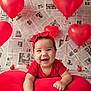 baby, smiling, red_clothing, headband, heart_shaped_pillow, red_balloons, heart_balloons, newspaper_background, indoor, portrait, cute, happy, infant, child, celebration, decor, festive, colorful, person, fun
