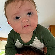 Jameson is registered to the contest to win money with this photo: baby, child, face, eyes, cheeks, hand, person, indoor, green_sleeves, clothing, hair, shoulders, tattoo, skin, portrait, cute, curious, young, holding, head