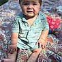 baby, child, outdoor, blanket, patterned_blanket, clothing, shorts, shirt, face, expression, sunlight, grass, picnic, toy, colorful, sitting, legs, feet, hand, skin