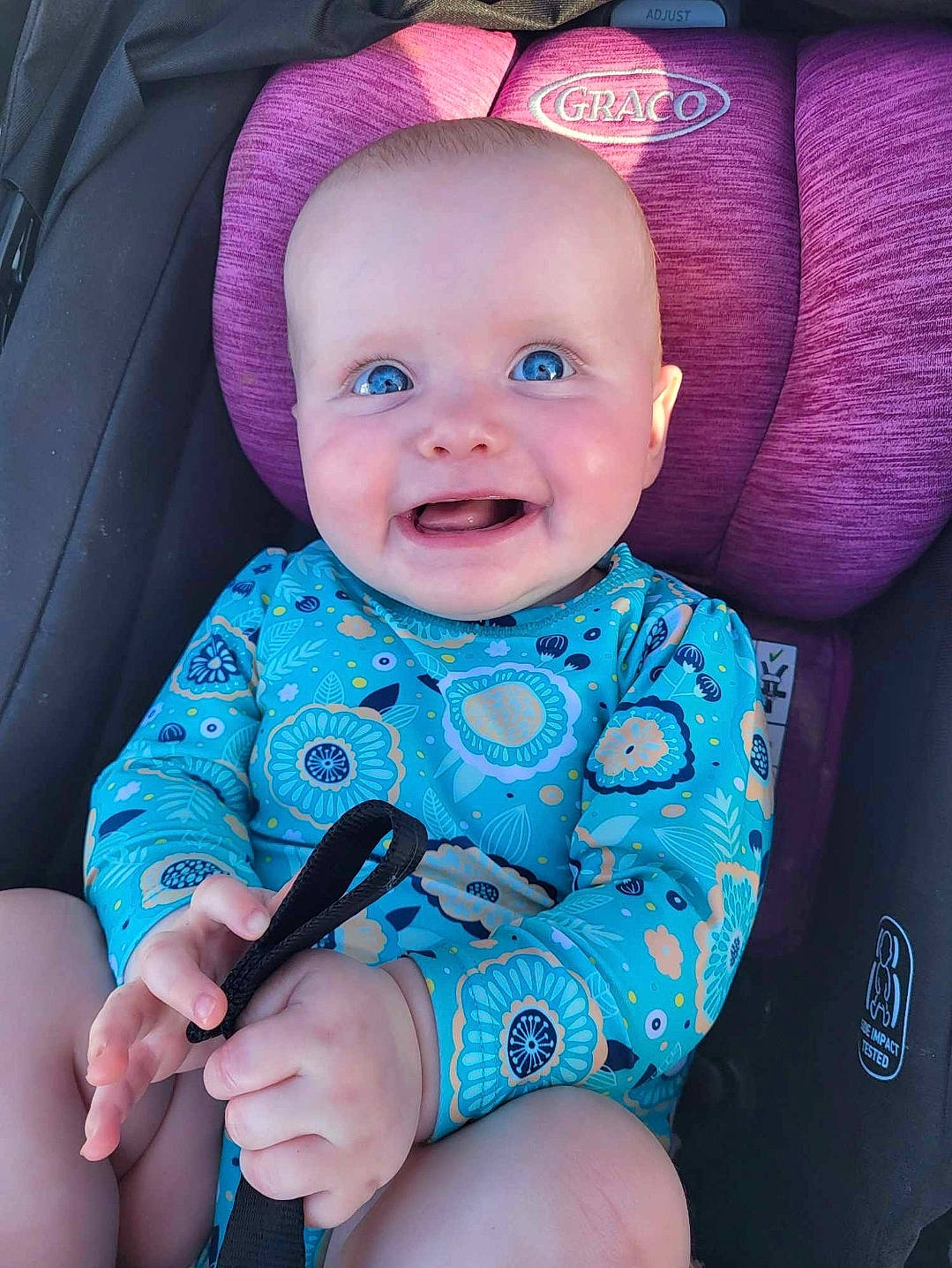 Riley is registered to the contest to win money with this photo: azure, baby, baby_toddler_clothing, cheek, chin, comfort, eye, facial_expression, finger, hand, human_body, joy, mouth, outerwear, person, pink, product, purple, seat_belt, skin