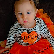 Paisley is registered to the contest to win money with this photo: child, toddler, baby, halloween, orange, black, bow, pumpkin, dress, striped_shirt, couch, sitting, costume, cute, face, person, footwear, indoor, holiday, festive