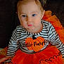 child, toddler, baby, halloween, orange, black, bow, pumpkin, dress, striped_shirt, couch, sitting, costume, cute, face, person, footwear, indoor, holiday, festive