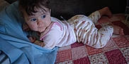 Paisley is registered to the contest to win money with this photo: baby, bed, blanket, blue_blanket, child, clothing, cozy, curly_hair, cute, face, hair, indoor, infant, looking_away, lying_down, pajamas, patterned_quilt, quilt, resting, soft_lighting