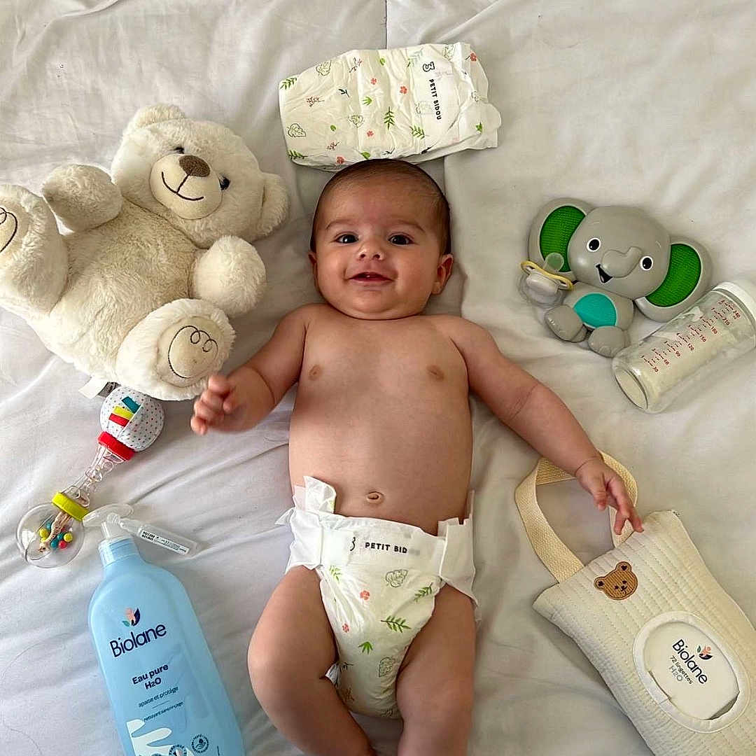 Nahyl a rejoint le concours — aidez-le/la à gagner de superbes lots ! baby, baby_lotion, baby_toys, bed, child, cute, diaper, happy, indoor, infant, lying_down, milk_bottle, nursery, person, skin, smiling, soft_toys, teddy_bear, toy_elephant, white_bedspread