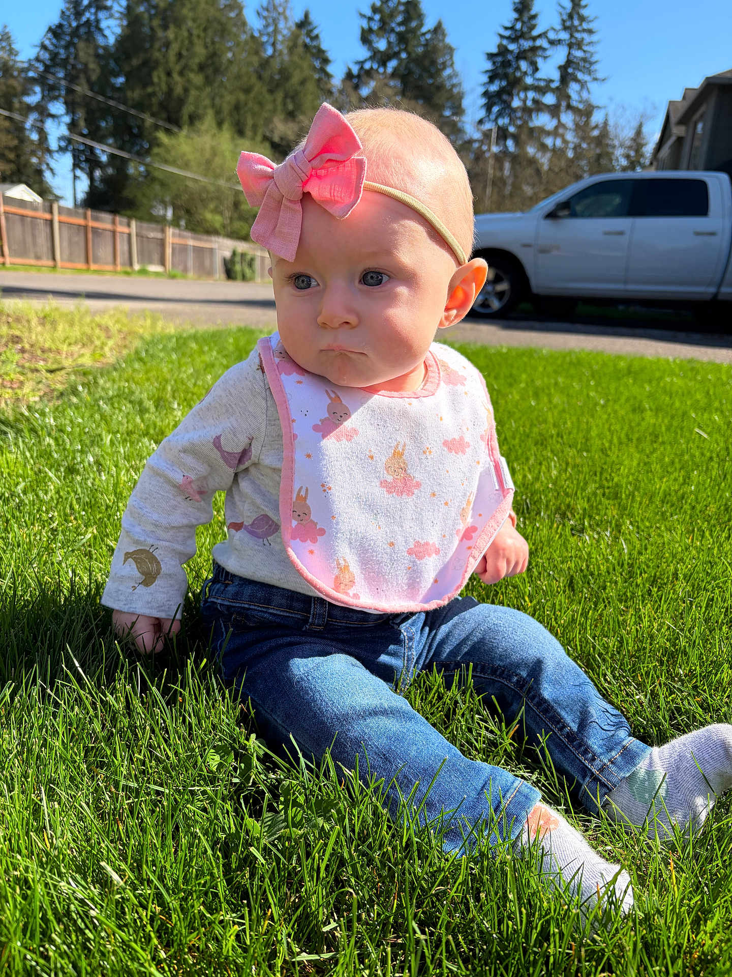 Lillian joined the competition — help win amazing prizes! baby, infant, child, headband, bow, bib, jeans, socks, grass, outdoors, sunlight, portrait, sitting, expression, cute, lawn, trees, fence, vehicle, daytime