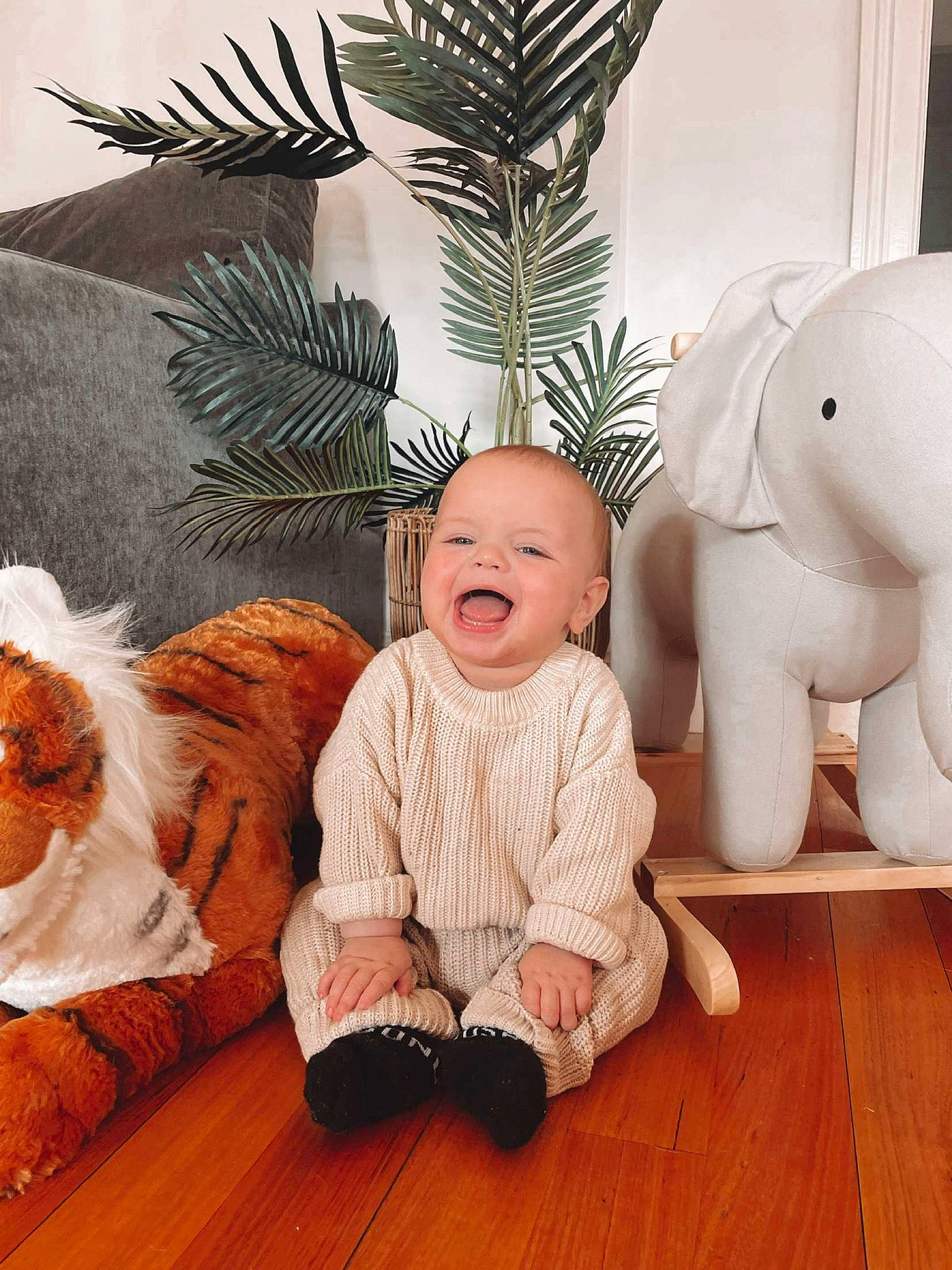 George is registered to the contest to win money with this photo: baby, baby_toddler_clothing, child, comfort, elephant, flooring, happy, hardwood, living_room, mammal, person, room, sitting, smile, stuffed_toy, textile, toddler, vertebrate, white, wood