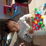 Noor participe au concours pour gagner de l'argent avec cette photo : child, toy, pegboard, colorful, smiling, indoor, table, wooden_floor, pigtails, play, sunlight, shadow, furniture, chair, mat, happy, cute, person, early_childhood, learning