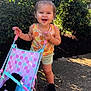 toddler, child, toy_stroller, stuffed_animal, outdoor, sunlight, greenery, happy, smiling, shorts, tank_top, black_shoes, hair_tied, playtime, nature, sidewalk, colorful, summer, polka_dots, cute