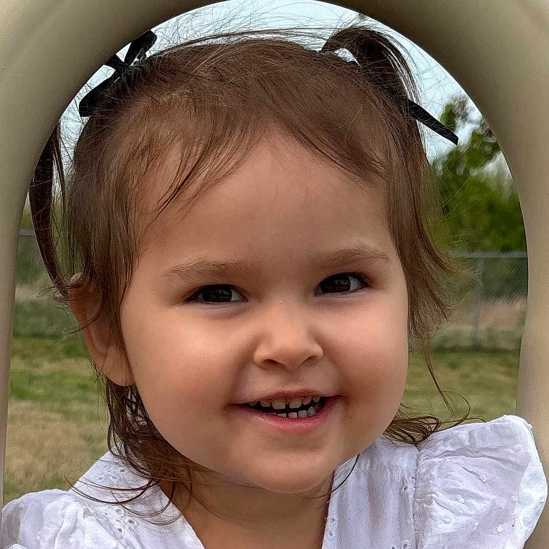 Devina is registered to the contest to win money with this photo: arch, baby, child, cute, daylight, eyes, face, grass, happy, head, nature, outdoor, person, pigtails, playground, portrait, smiling, toddler, white_dress, young_child