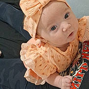 Oaklynn is registered to the contest to win money with this photo: baby, infant, child, portrait, close_up, bow, headband, peach_outfit, dress, smiling, looking_at_camera, blue_eyes, sitting, indoors, lap, adult, blanket, couch, casual, family