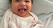 Vanessa is registered to the contest to win money with this photo: baby, infant, tongue_out, pink_clothing, cute, playful, bed, blanket, soft, smiling, expression, portrait, indoors, child, young, person, hair, face, sleepwear, cozy