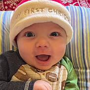 Makai is registered to the contest to win money with this photo: baby, infant, smiling, face, hat, christmas, holiday, pajamas, striped_pillow, background, red, white, green, blue, pattern, closeup, child, cute, happy, indoors