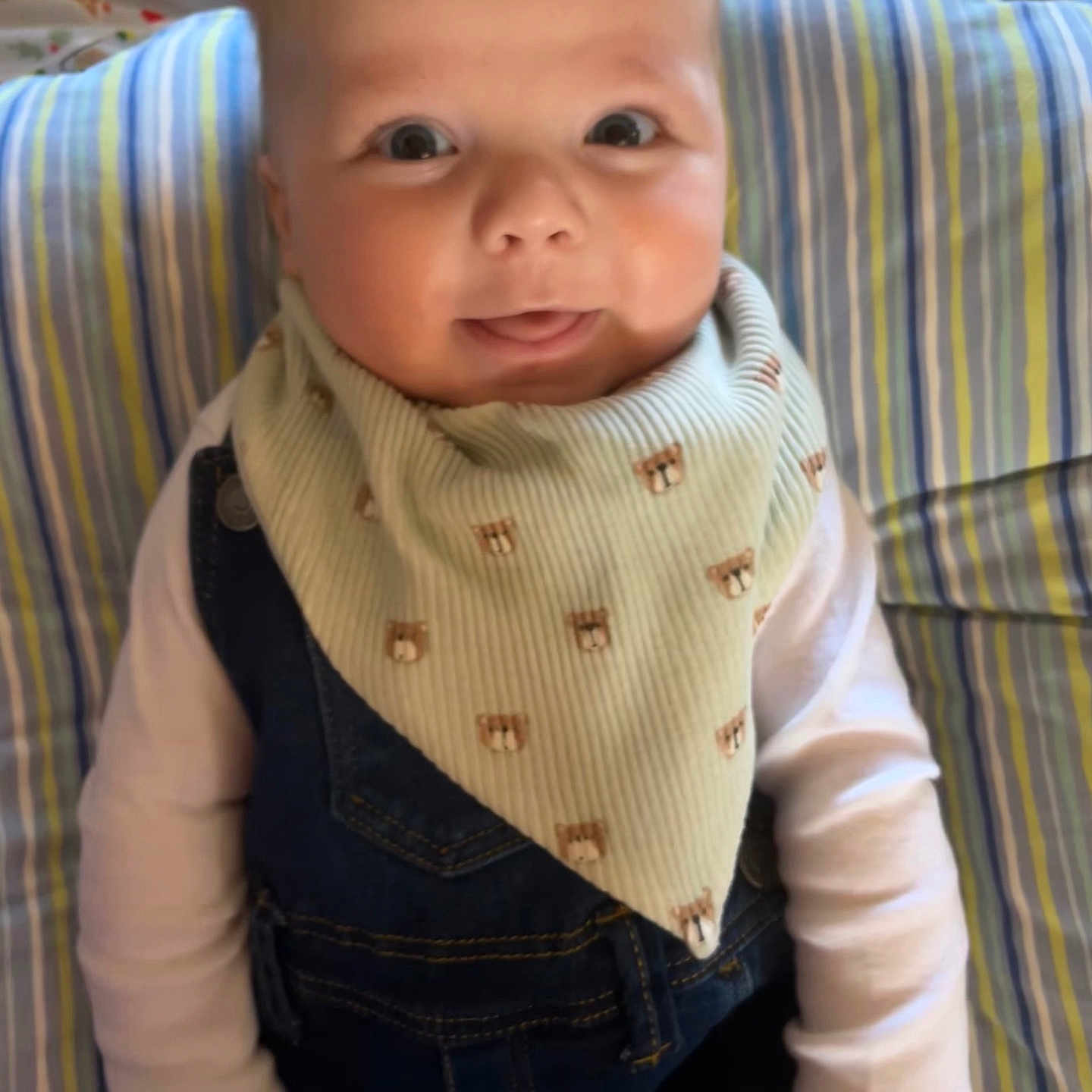 Makai is registered to the contest to win money with this photo: baby, background_pattern, bib, child, clothing, cute, denim_overalls, face, hands, happy, head, indoors, infant, person, portrait, seated, smiling, striped_cushion, tongue_out, young_child