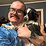 Big Ed joined the competition — help win amazing prizes! man, dog, glasses, mustache, tattoo, watch, smile, hug, indoor, blue_shirt, black_and_white_dog, short_hair, person, background, doorway, casual, happy, pet, friendship, home