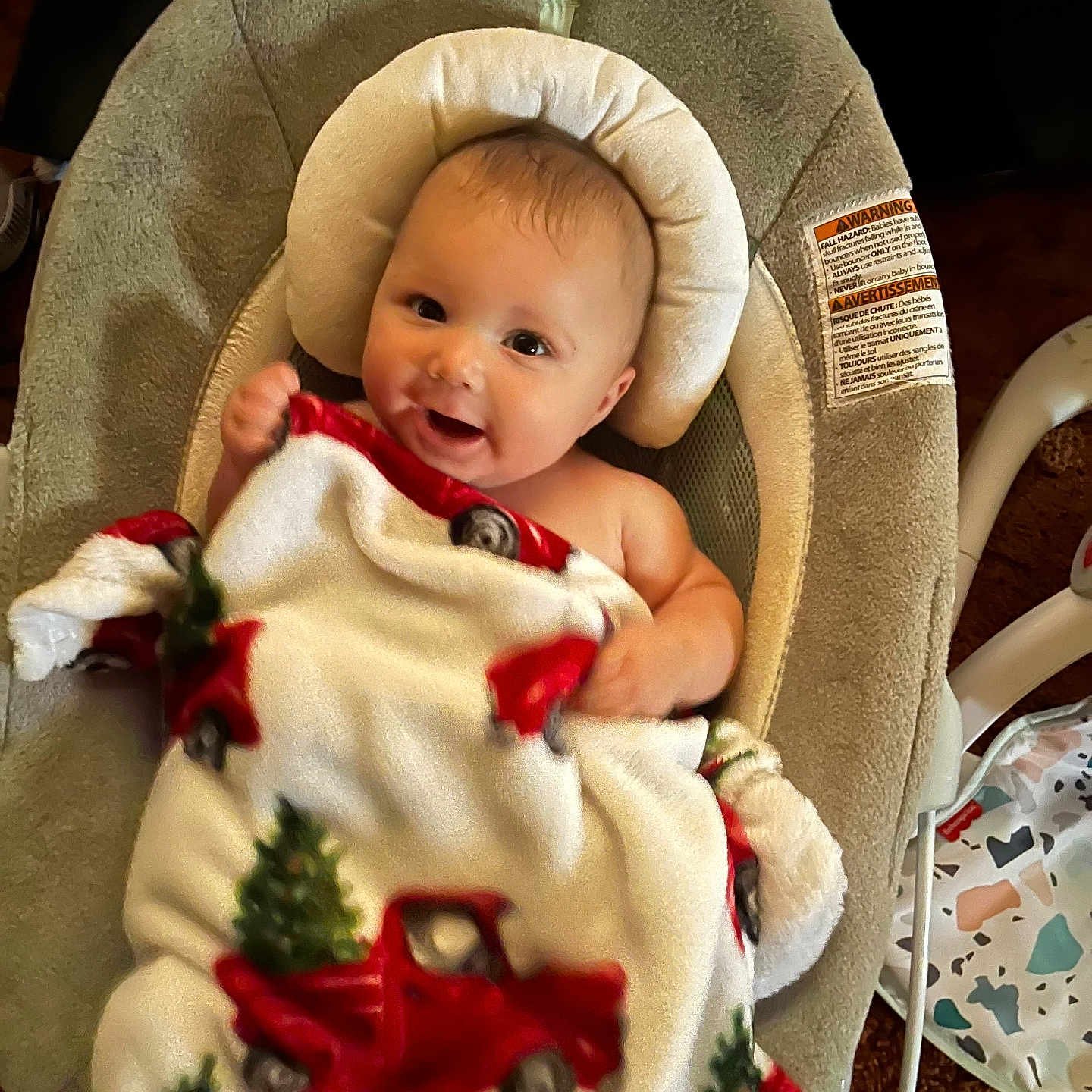 Jerrold joined the competition — help win amazing prizes! baby, baby_seat, blanket, carpet, child, christmas_tree, comfort, cozy, cushion, cute, face, happy, head_support, indoors, infant, person, red_truck, smile, warm, wrapped