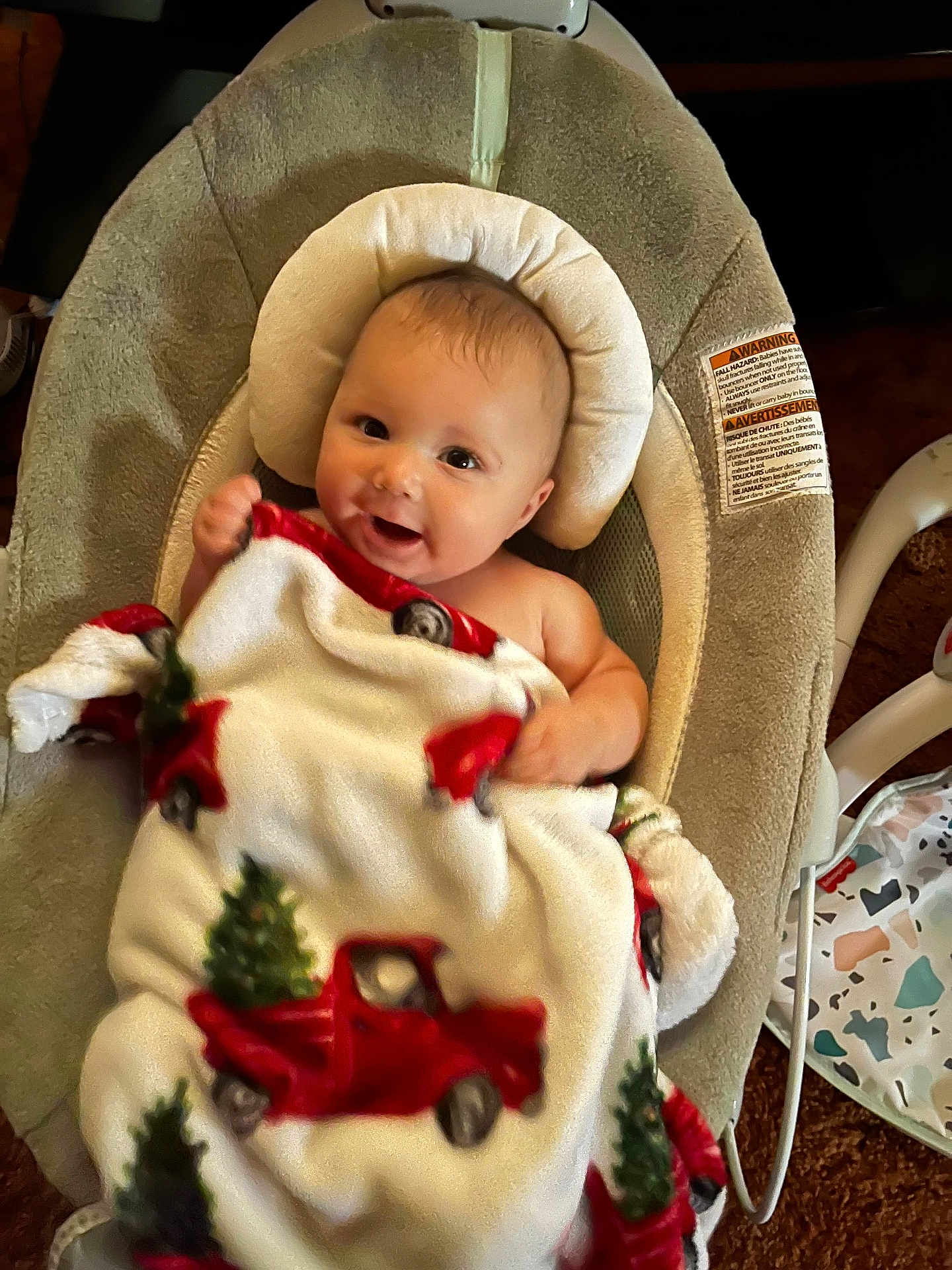 Jerrold joined the competition — help win amazing prizes! baby, baby_seat, blanket, carpet, child, christmas_tree, comfort, cozy, cushion, cute, face, happy, head_support, indoors, infant, person, red_truck, smile, warm, wrapped