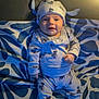 baby, infant, child, pajamas, hat, cute, smiling, face, patterned_blanket, pillow, indoor, cozy, soft_light, blue, white, sitting, clothing, foot, portrait, expression